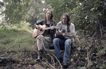 Gillian and Dave with their guitars in the woods.